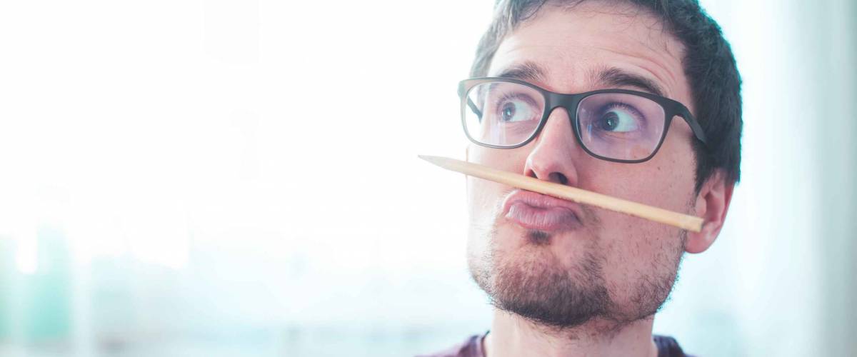 Young Caucasian man is fooling around and home, pencil trapped between nose and lips