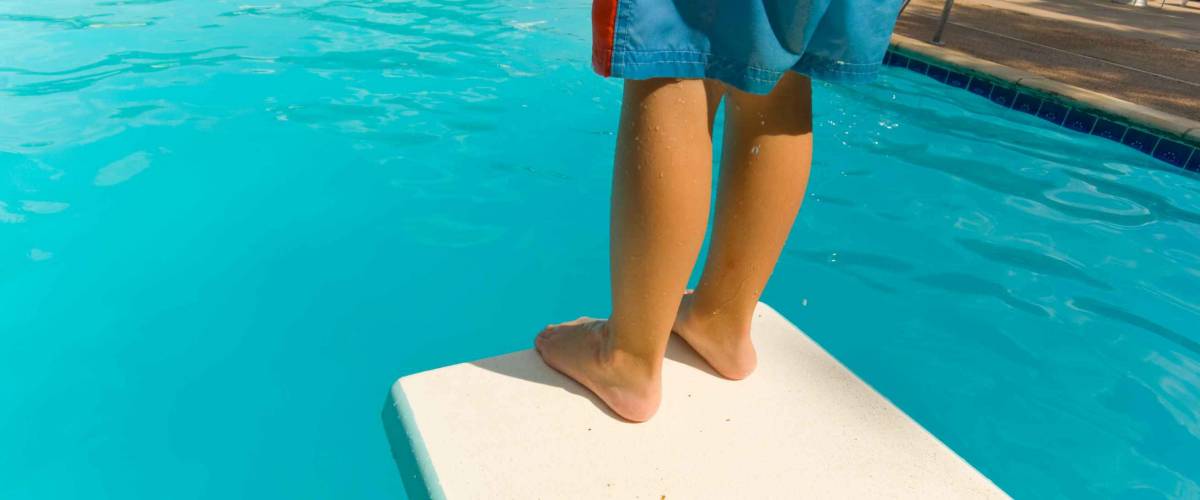 Young boy standing on the end of a diving board at a swimming pool - seems to be a little apprehension