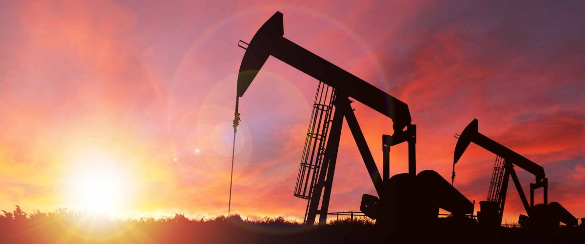 Pumpjack silhouette against a sunset sky with deliberate lens flare and copy space. These jacks can extract between 5 to 40 litres of crude oil and water emulsioin at each stroke.