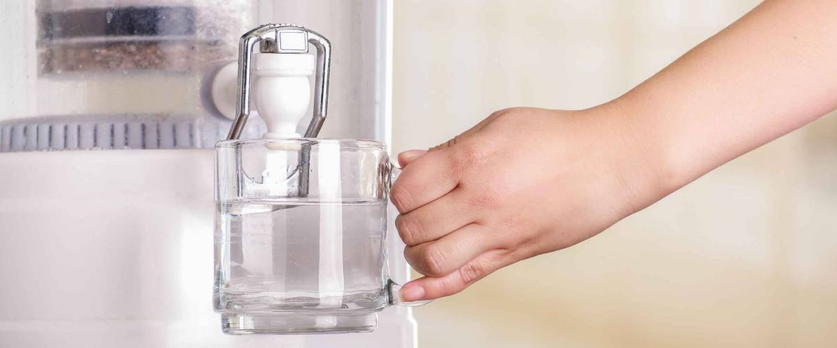 Close up of a woman filling a glass of water, with a filter system of water purifier on a kitchen background