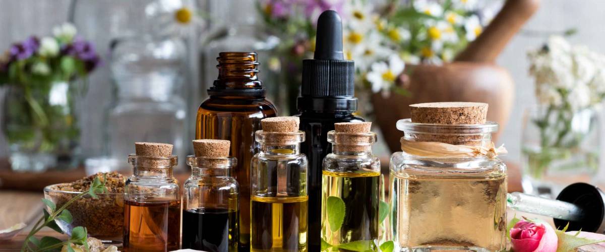 Selection of essential oils, with herbs and flowers in the background