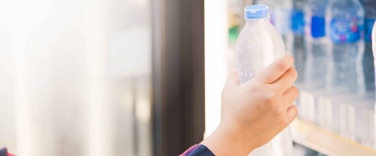 woman choosing cold bottle of water or beverage on shelves in supermarket store.