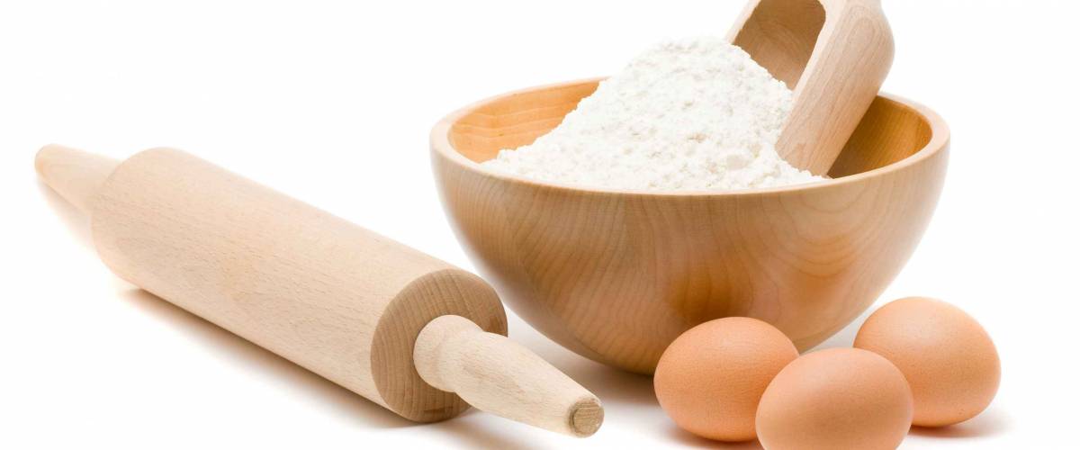 Baking ingredients - flour in bowl with eggs and rolling pin over white background
