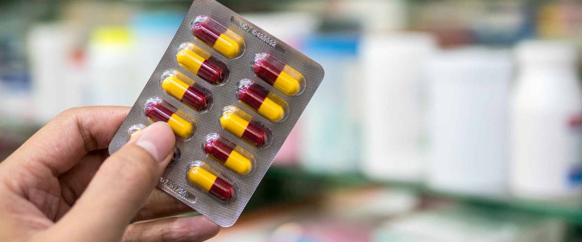 Hand holding medicine yellow and brown colour capsule pack in pharmacy drugstore.