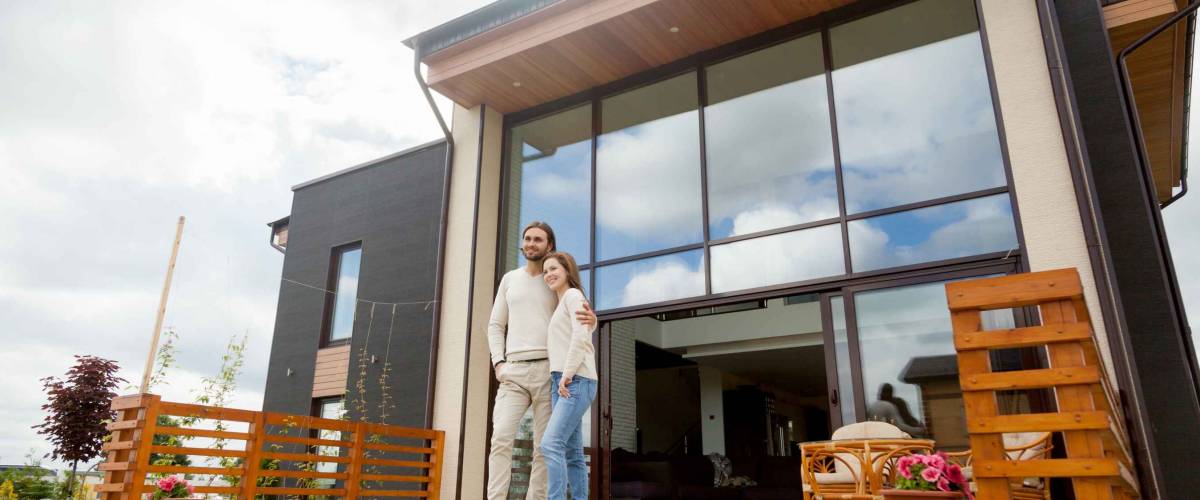 Happy young couple embracing standing outside big house on front porch after refinancing