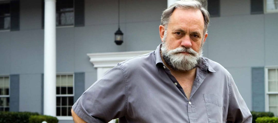 Unhappy homeowner poses in front of his two story columned southern home.