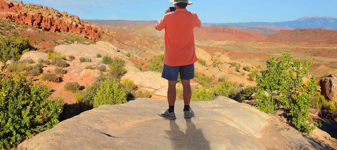 Man standing on top of the mountain taking photos ,looking at beautiful autumn mountains landscape. Moab, Utah, Arches National Park.