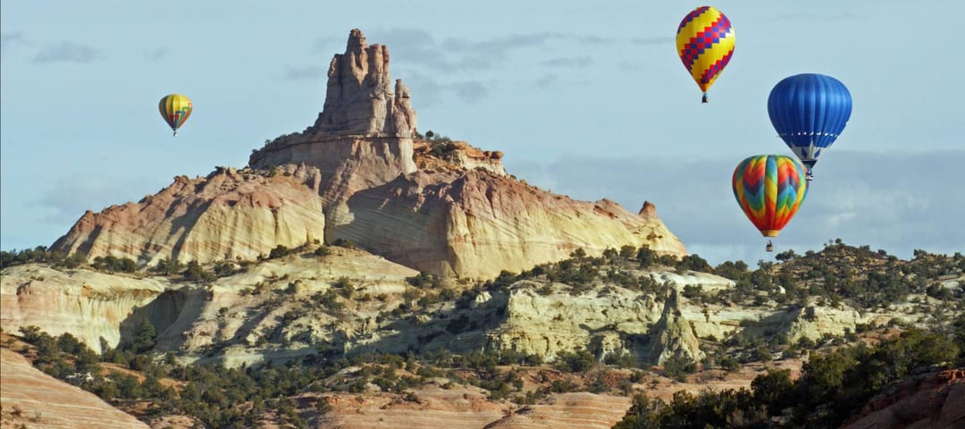 A group of hot air balloons rise above the red sandstone of Red Rocks State Park near Gallup, New Mexico, and circle around the Church Rock formation