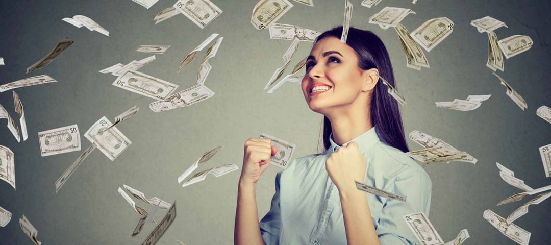 Portrait happy woman exults pumping fists ecstatic celebrates success under a money rain falling down dollar bills banknotes isolated on gray wall background with copy space