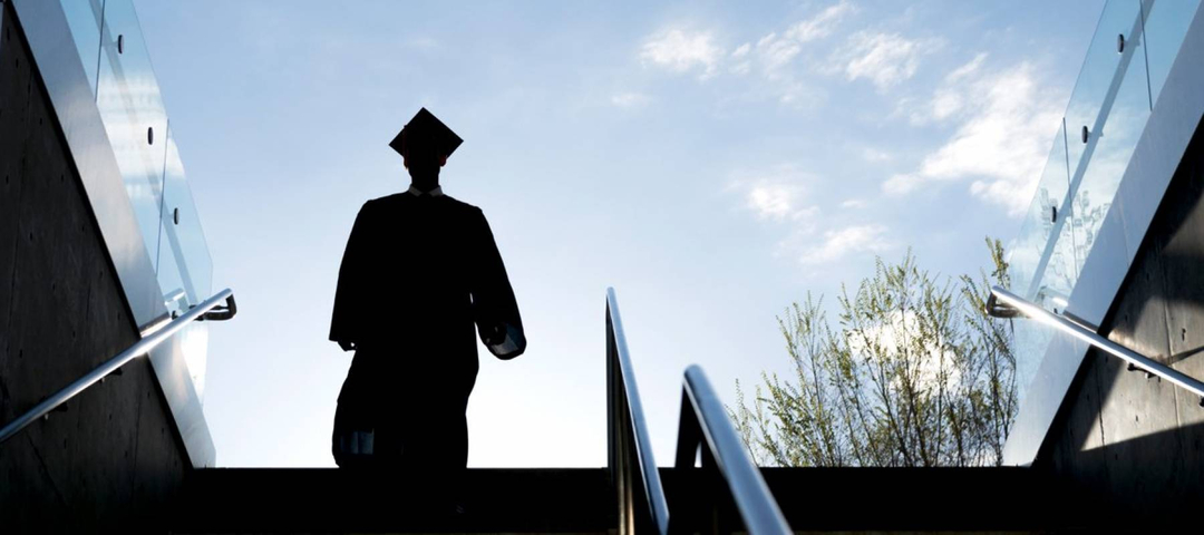 College graduate in silhouette wearing cap and gown and descending a stairway into a subway or underground garage