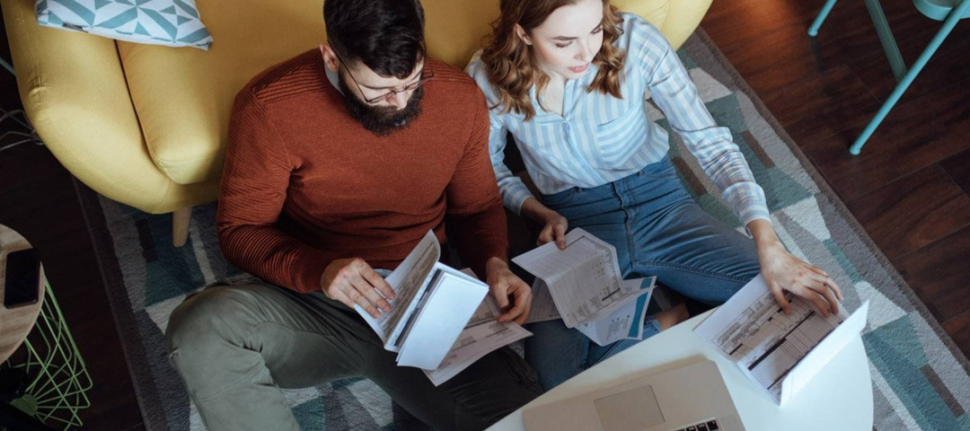 Bearded man and woman with curly hair discuss bills in photo shot from overhead