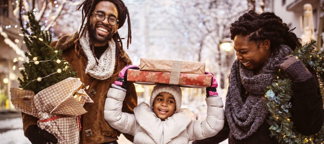 Black family (father, child and mother) bringing home small Christmas tree and packages