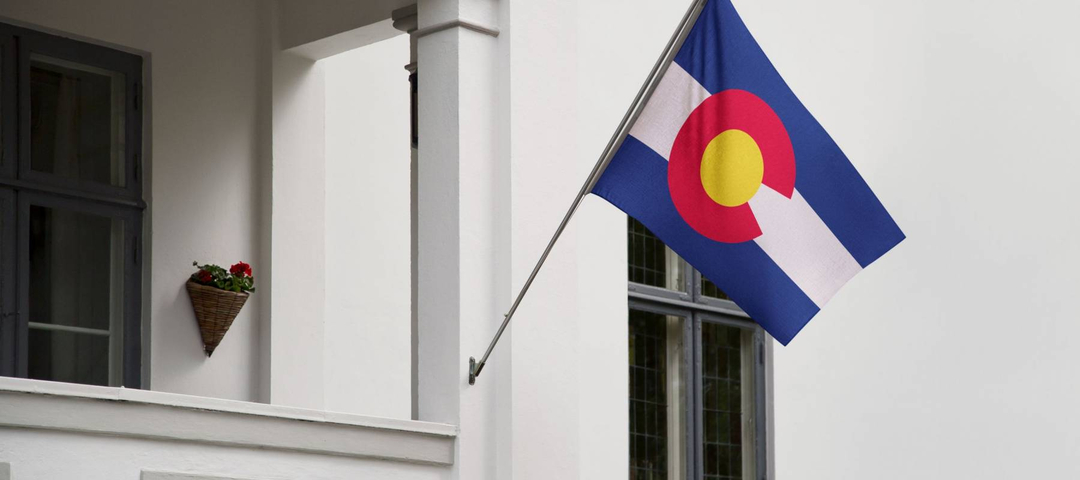 Colorado flag. Colorado state flag hanging on a pole in front of the house. State flag waving on a home displaying on a pole on a front door of a building. Flag raised at a full staff.