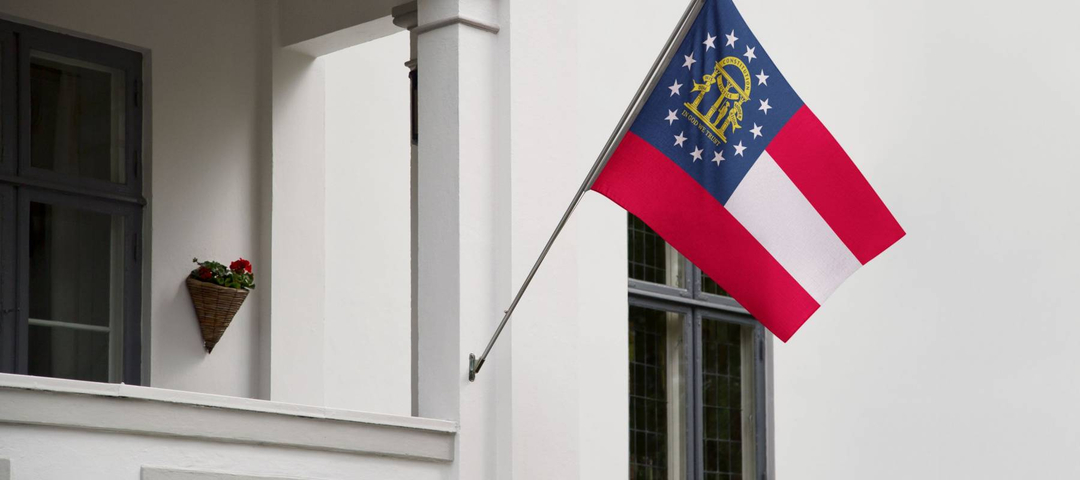 Georgia flag. Georgia state flag hanging on a pole in front of the house. State flag waving on a home displaying on a pole on a front door of a building. Flag raised at a full staff.