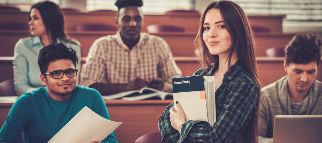 Multinational group of cheerful students taking an active part in a lesson while sitting in a lecture hall.