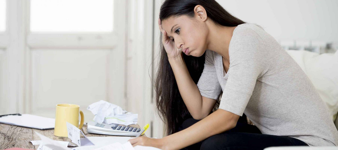 young hispanic woman at home living room couch calculating monthly expenses worried in stress with bank papers and documents in paying taxes , mortgage debt and cost of living concept
