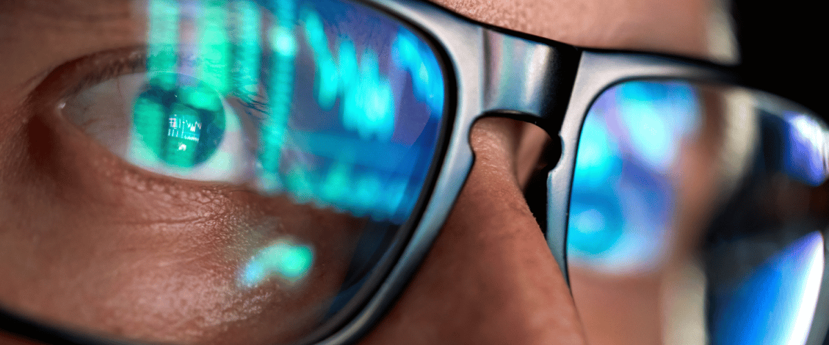 Focused crypto trader analyst wearing eyeglasses working looking at computer screen reflecting in glasses analyzing online trading stock exchange market data charts. Close up eye reflection.