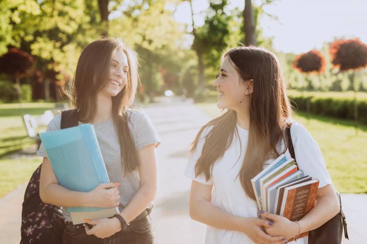 Two happy student girls walking and talking to each other on campus.