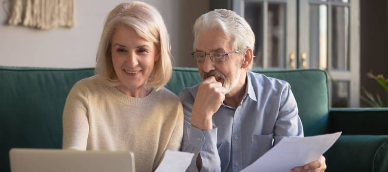 Happy older couple holding documents and looking at computer screen