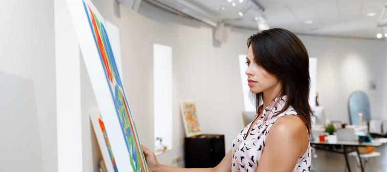 Young caucasian woman standing in an art gallery in front of painting displayed on white wall