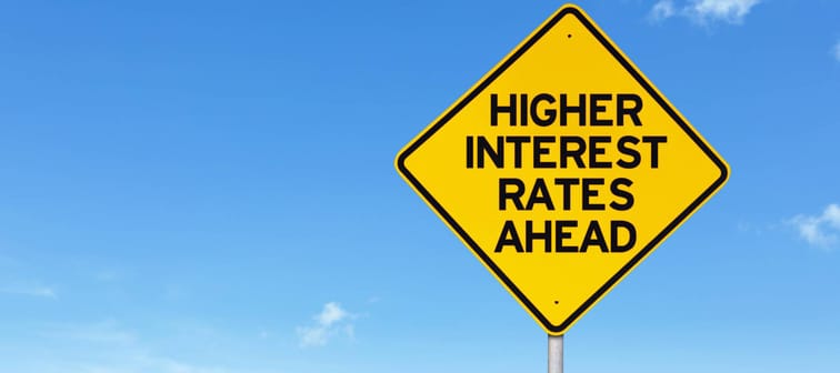 Higher interest rate road sign against empty field and blue sky