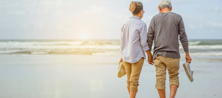 Senior couple walking along a beach, holding hands.