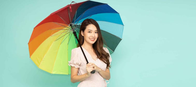 Young Asian woman holding rainbow umbrella isolated on green background, In the rainy season concept