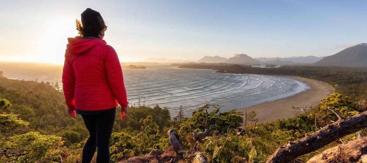 Adventurous Woman Hiker overlooking Sandy Beach on the West Coast of Pacific Ocean. Canadian Nature Landscape Background. Cox Bay Lookout, Tofino, Vancouver Island, BC, Canada.