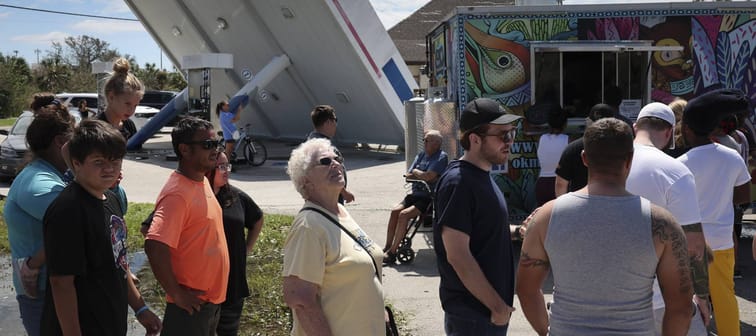 Residents line up for free food being distributed from a taco truck at a gas station destroyed by Hurricane Ian in Port Charlotte, Fla., Sept. 29, 2022.