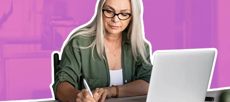 an older woman with long grey hair sitting in front of an open laptop