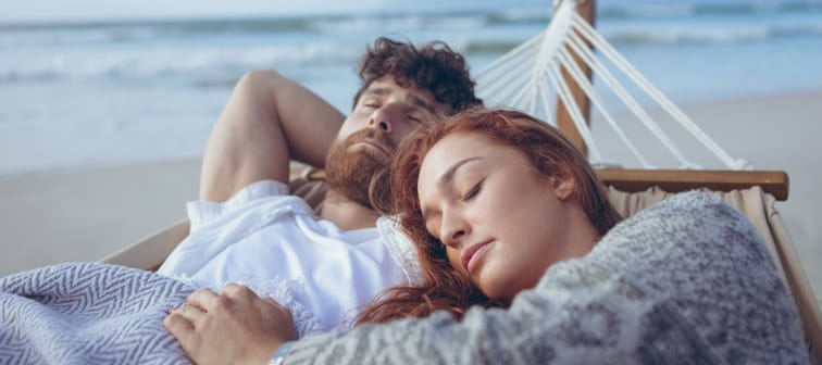 A young couple lay in a hammock by the beach.