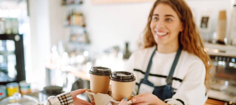Barista holding take away coffee in a tray for a customer, smiling.