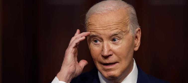 President Biden seen in close up, holding one hand to the side of his face while in the middle of speaking.