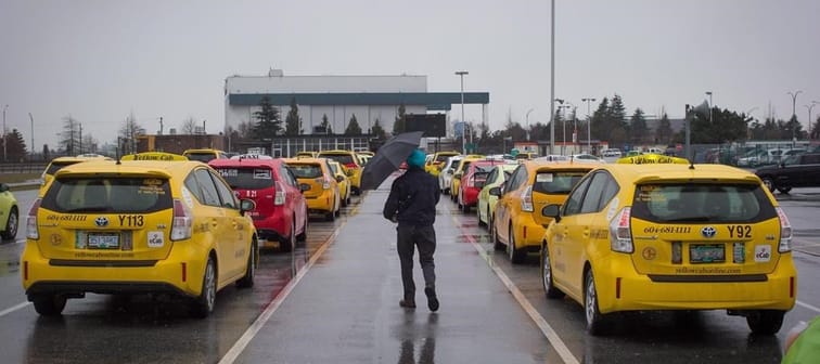 A taxi driver walks past cabs while waiting for passengers at Vancouver International Airport, in Richmond, B.C., on Tuesday March 7, 2017. 