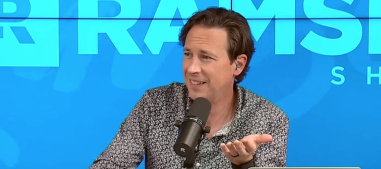 Man with grey hair sitting on radio show set, making incredulous face.