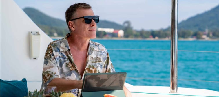 Businessman wearing sunglasses while working on digital tablet on a boat while on a tropical vacation