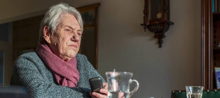 Older woman sits lost in thought with a cup of tea at her dining table.