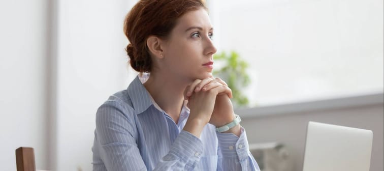 Lost in thoughts woman sits at workplace desk in office in front of laptop