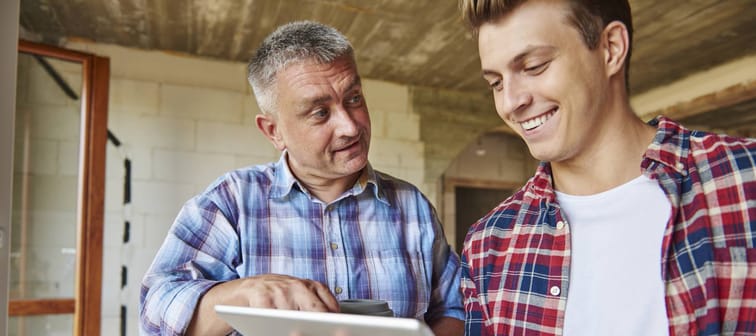 Older man points to tablet, talking to younger man.