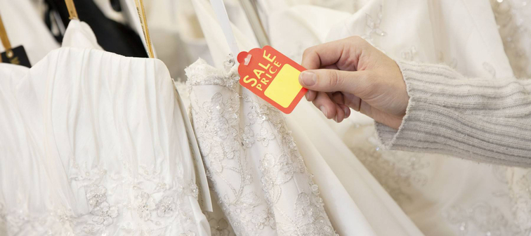 Cropped shot of female hands holding price tag attached to wedding gown in bridal boutique