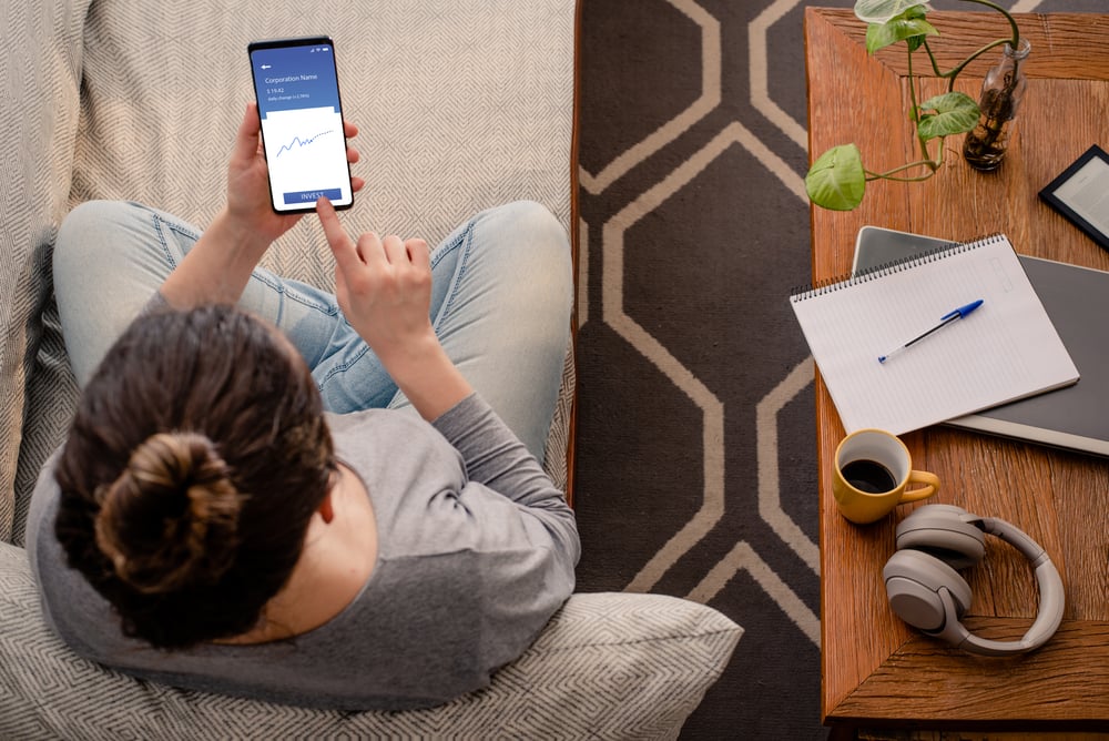 Woman sitting on couch using mobile phone to look at investments