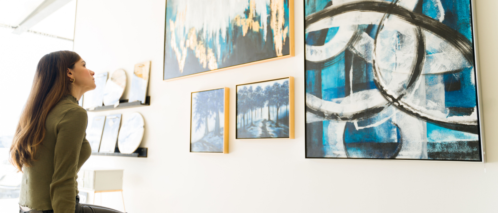 Side view of a woman studying and watching the abstract paintings and colorful canvases during a visit to the art gallery