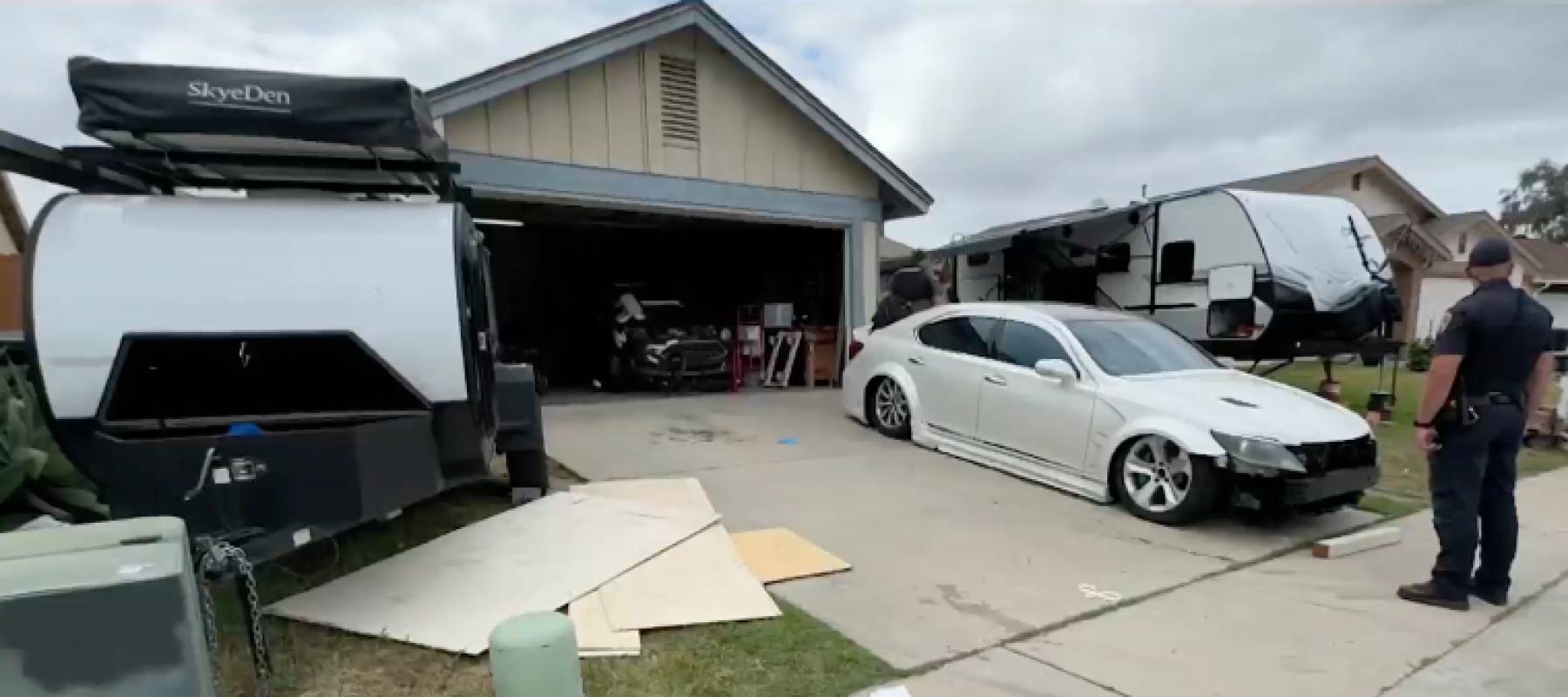 A police officer stands in front of a house with two trailers.