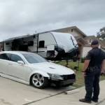 A police officer stands in front of a house with two trailers.