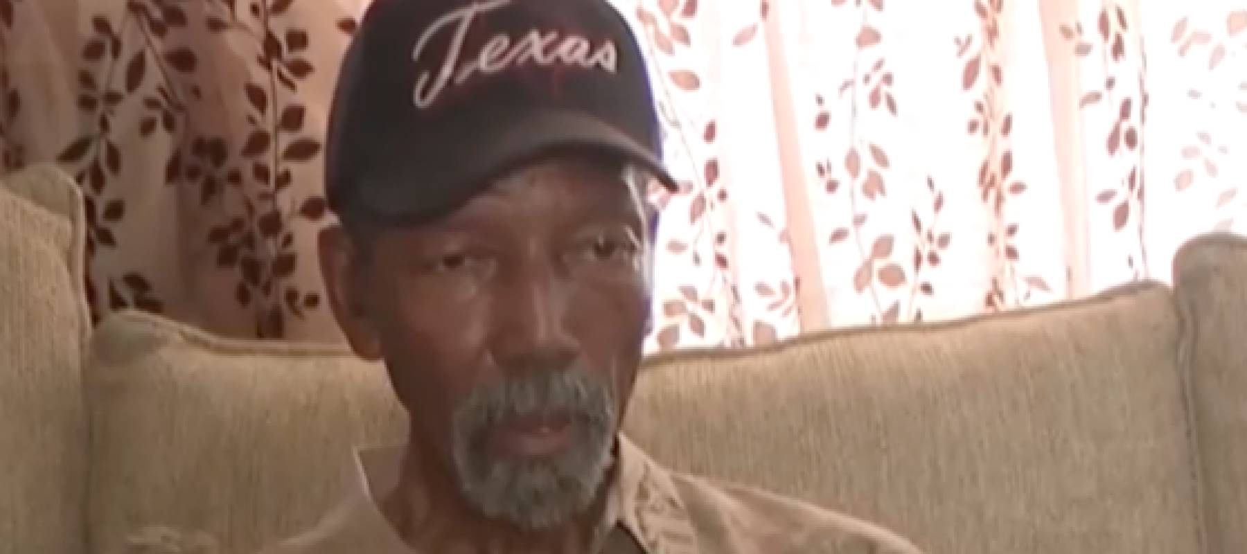 Man sits on a couch talking to a reporter.