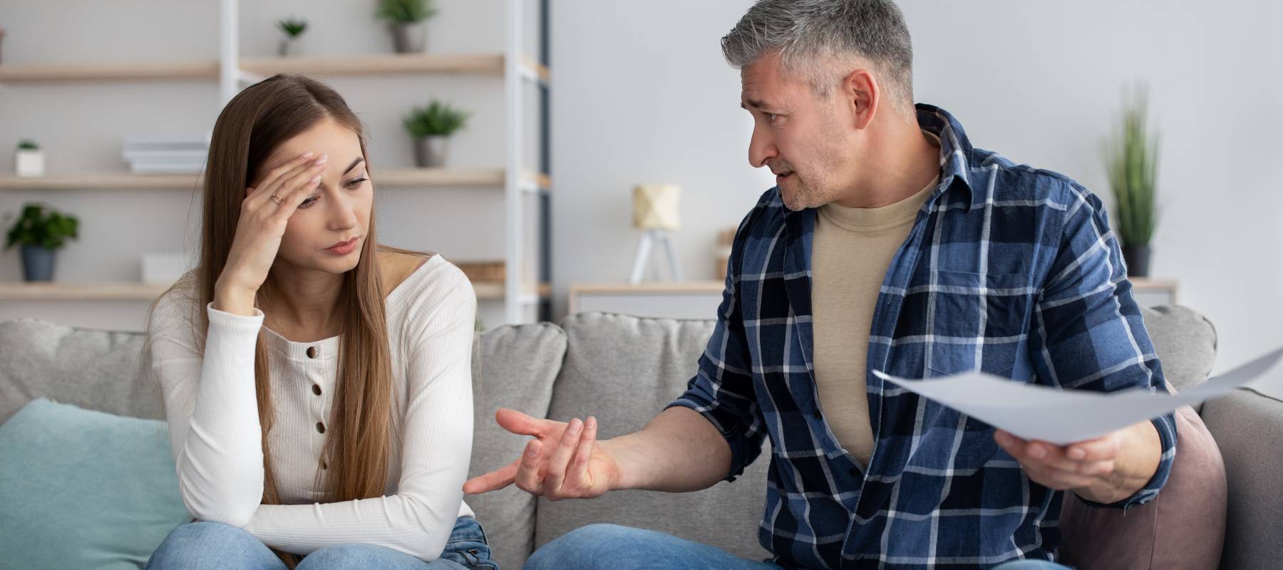 Woman holding her head sitting next to older man on couch.