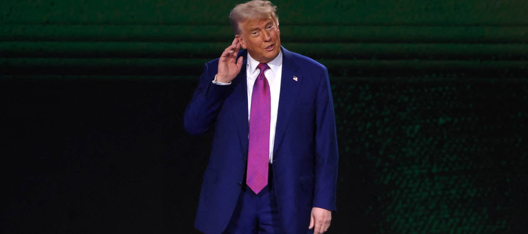 Donal Trump holds his hand to his ear on stage.