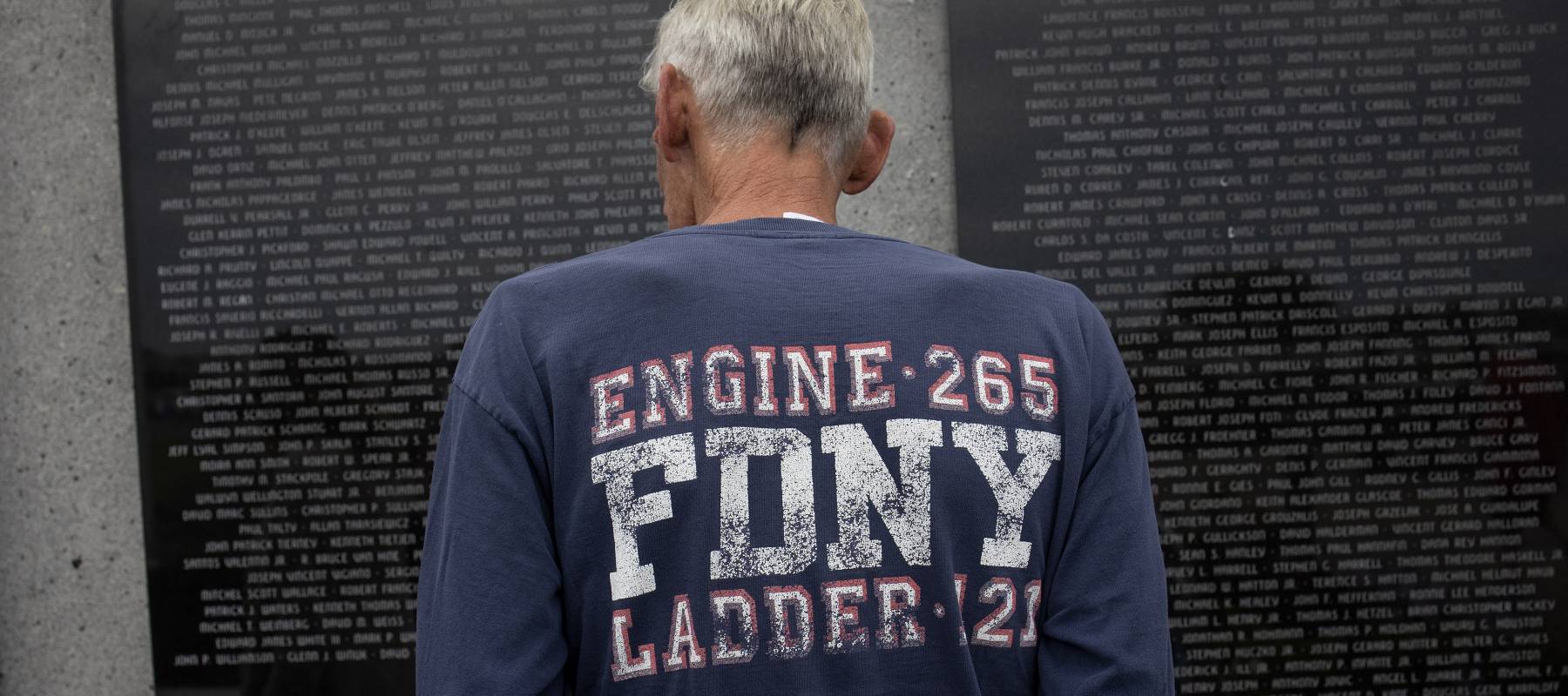 A man wearing an FDNY  t-shirt satnds in front of a 9/11 memorial.