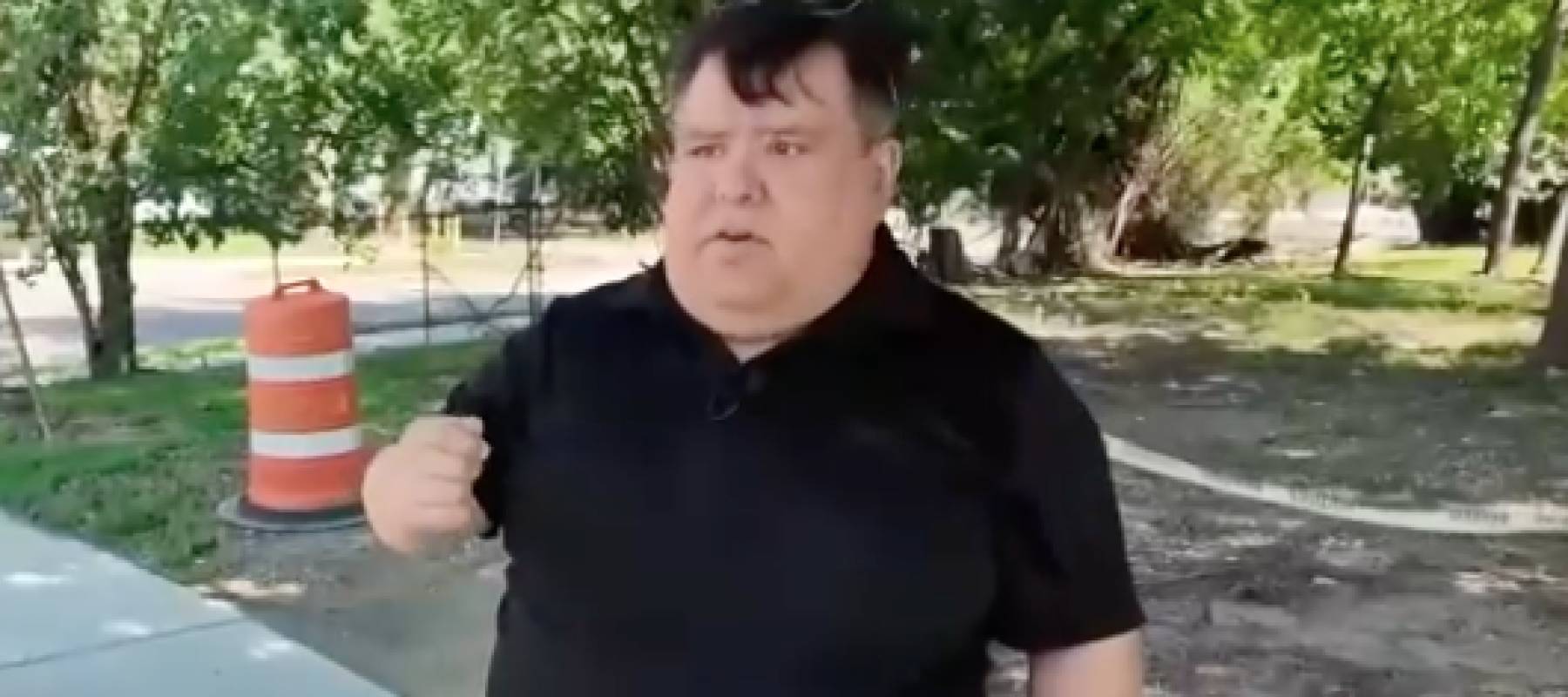 Man speaks to reporter in front of dirt driveway.