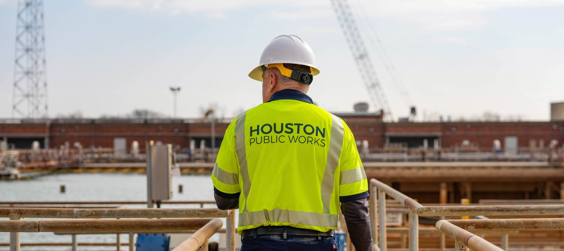 A worker with a yellow Houston Public Works vest and a hard hat walking in front of the photographer.
